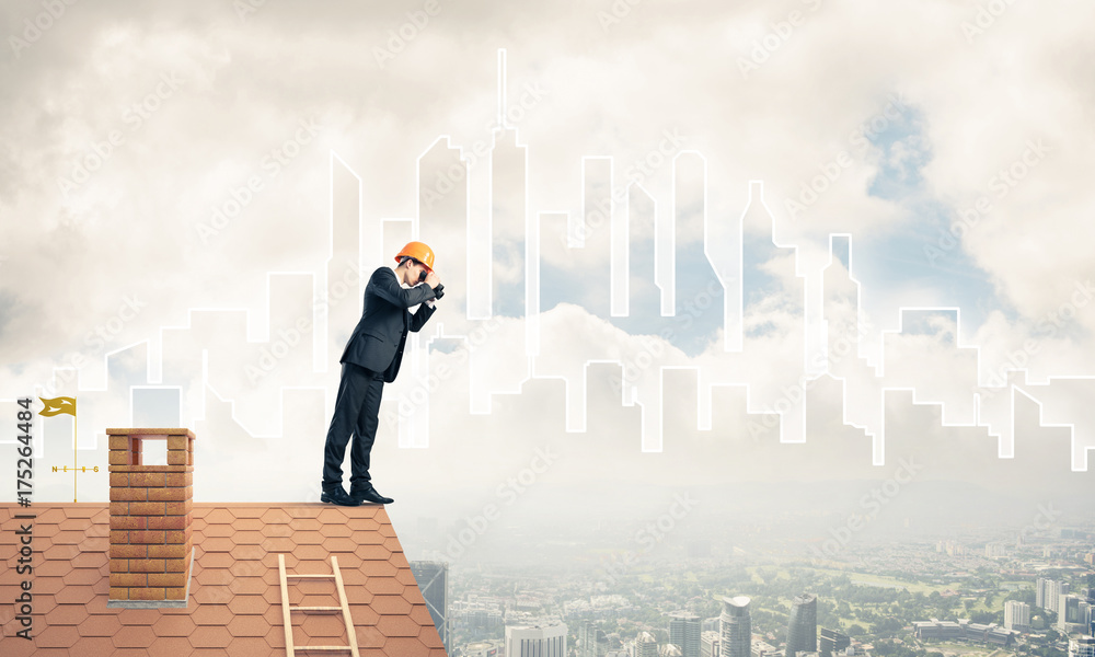 Engineer man standing on roof and looking in binoculars. Mixed m