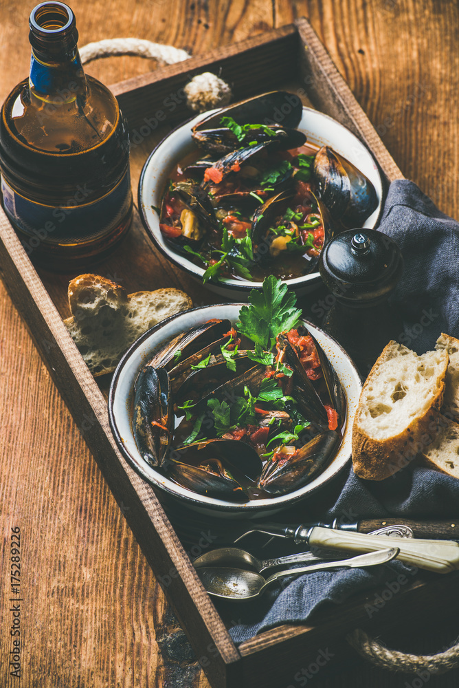 Belgian boiled mussels in tomato sauce with fresh parsley in serving metal bowls and baguette bread 