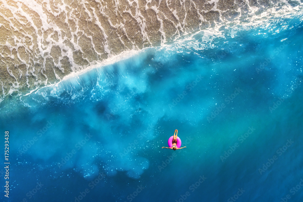 Aerial view of young woman swimming on the pink swim ring in the transparent turquoise sea in Oluden