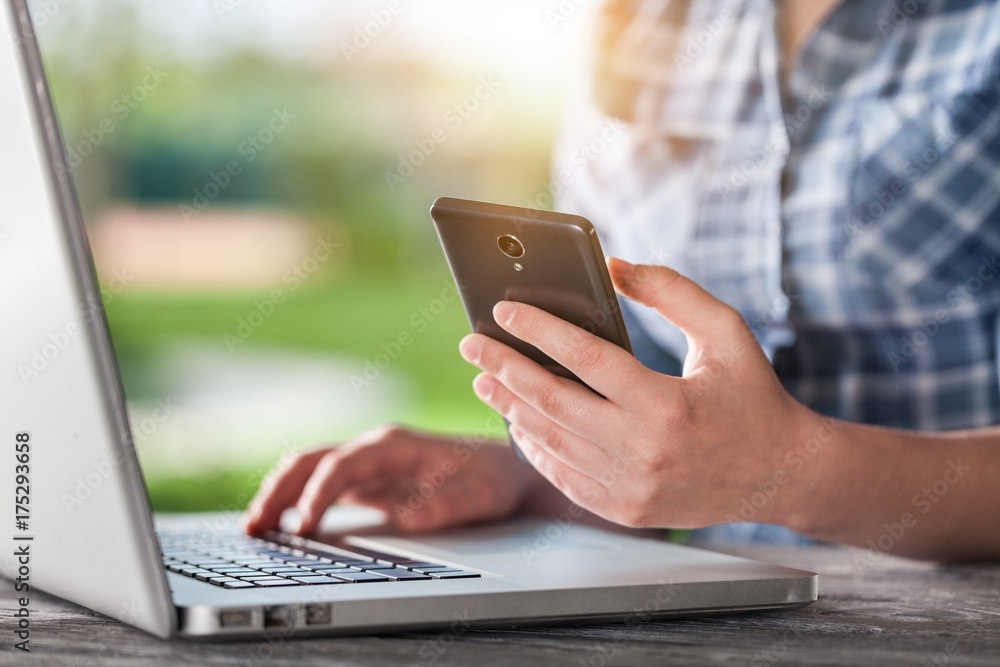 Human with phone works on laptop.