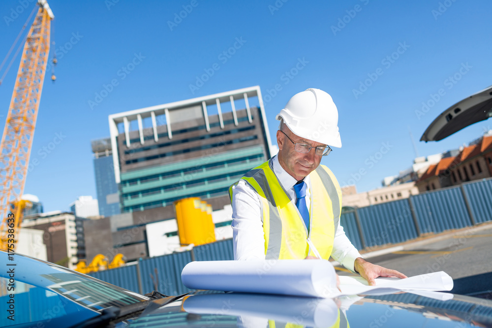 戴眼镜的高级工头在汽车引擎盖上的建筑区域工作