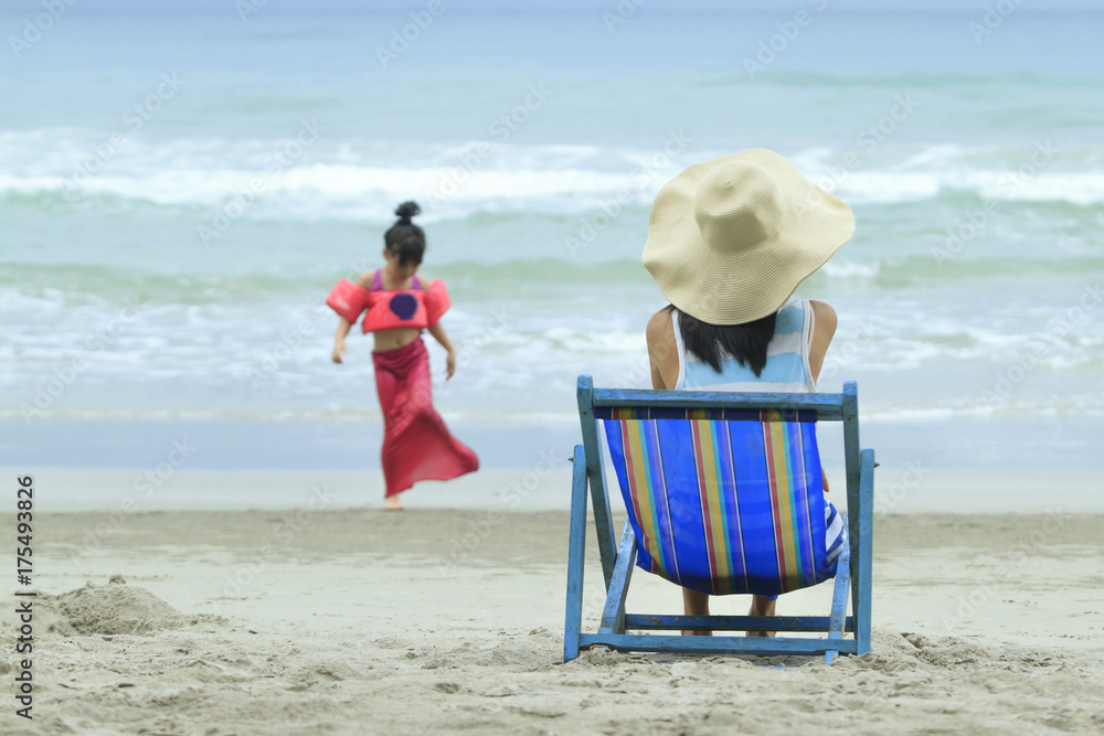 母亲坐在海滩上的躺椅上，看着女儿玩耍，家庭生活方式旅行健康