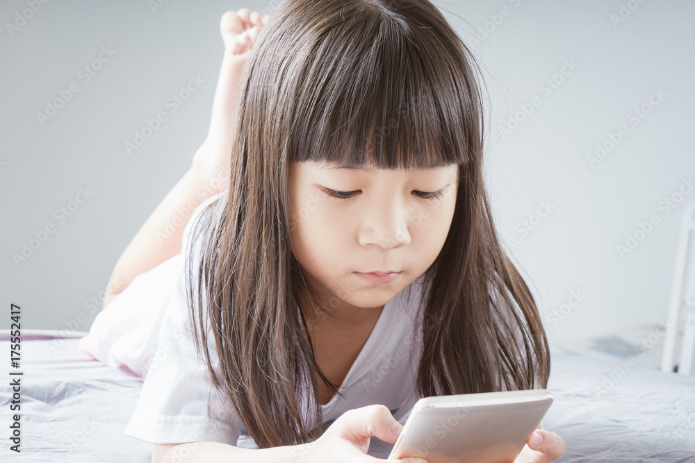 Little asian  girl using smartphone and lying on the bed . child addicted phone.