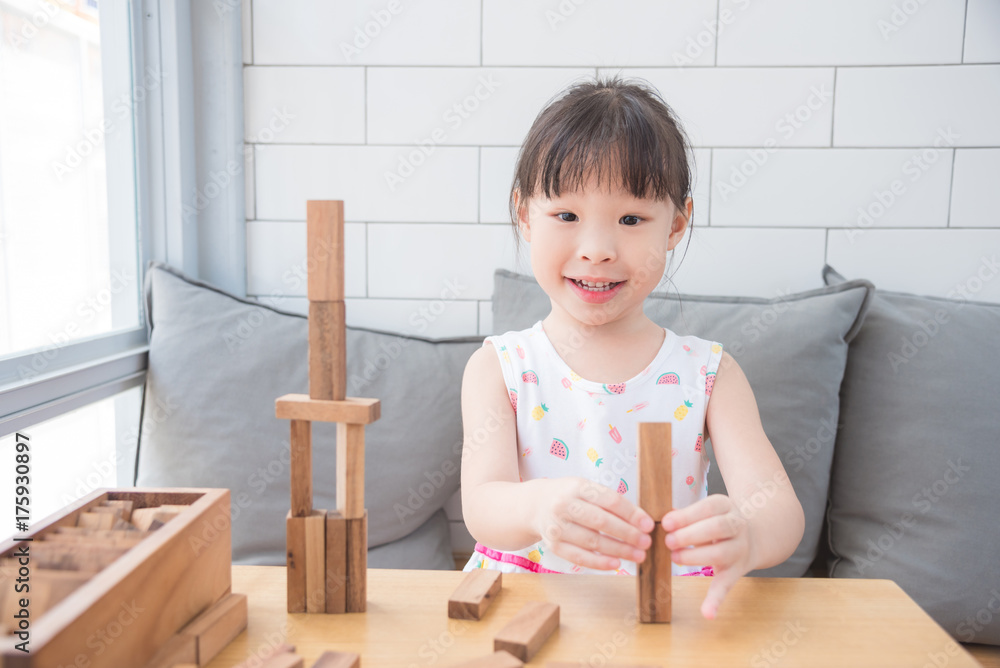 Little asian girl smiling while playing wooden blocks on table in living room