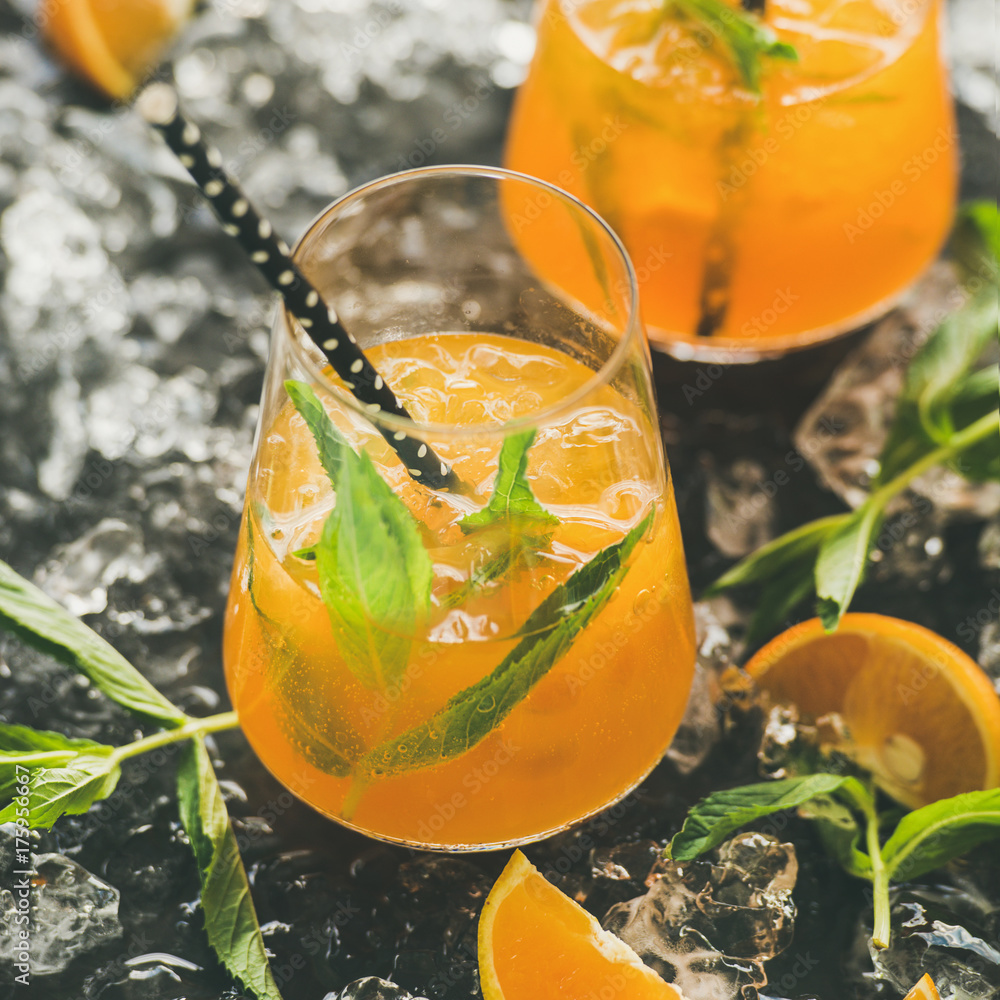 Refreshing cold alcoholic summer citrus cocktail with orange, peppermint and ice in stemless glasses