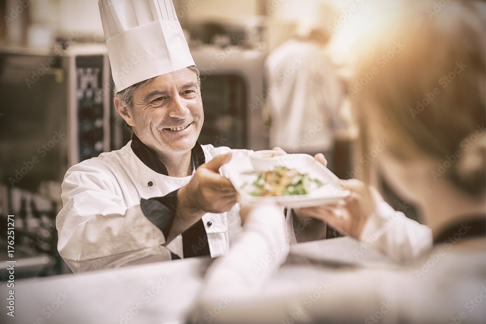 Chef handing dinner dish to waitress at order station