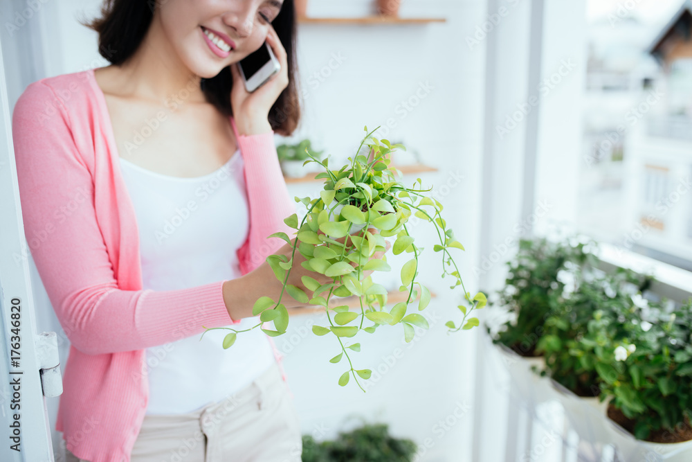 Charming Young Asian Woman Watering Plant In Container On Balcony Garden