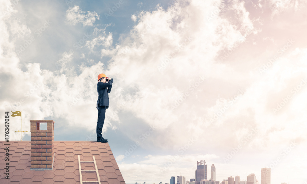 Engineer man standing on roof and looking in binoculars. Mixed m