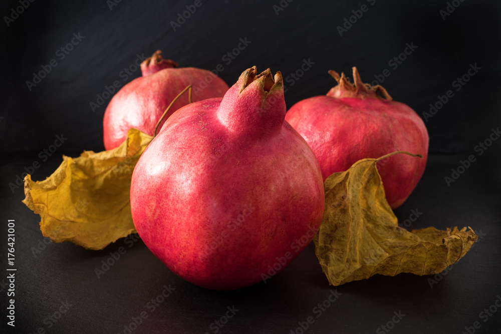 Fresh pomegranate with leaves close up on black background