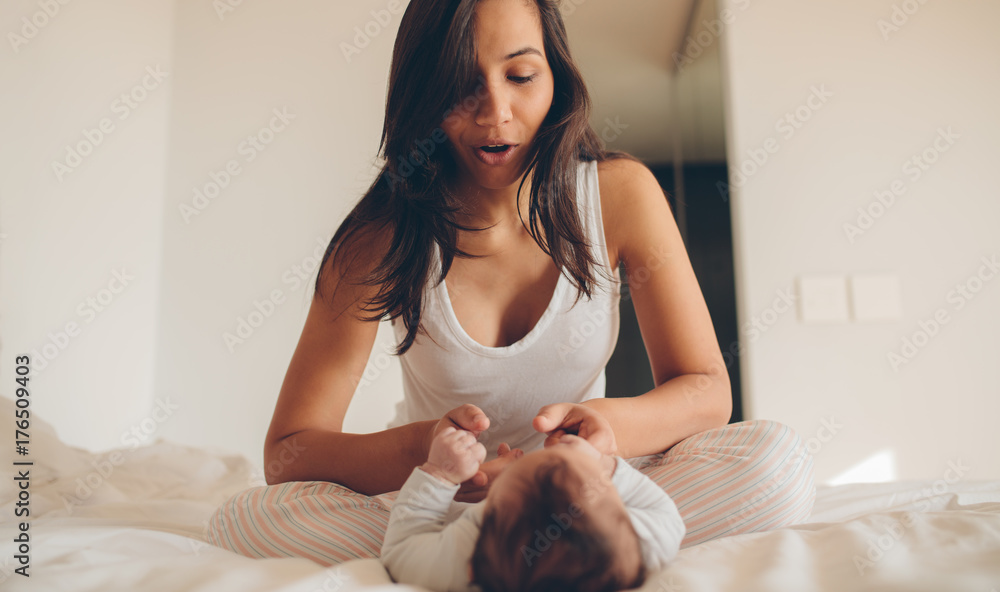 Woman sitting on bed and playing with her baby