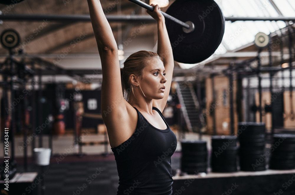 Focused young woman lifting heavy weights in a gym