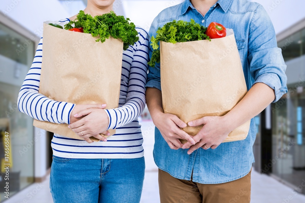 Composite image of mid section of couple holding grocery bags