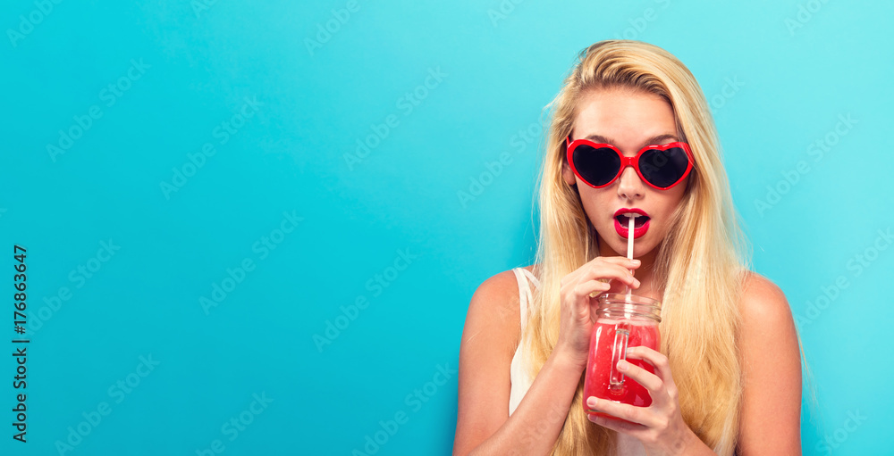 Happy young woman drinking smoothie on a solid background