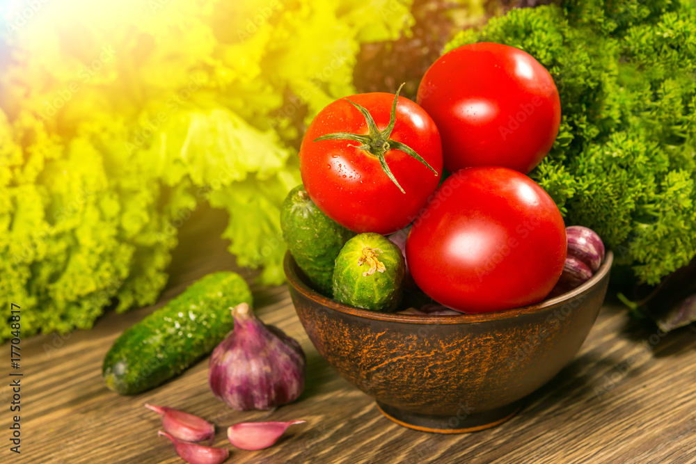 Tomatoes, garlic bulb and cucumbers on a wooden table. Green salad in the background. The concept of