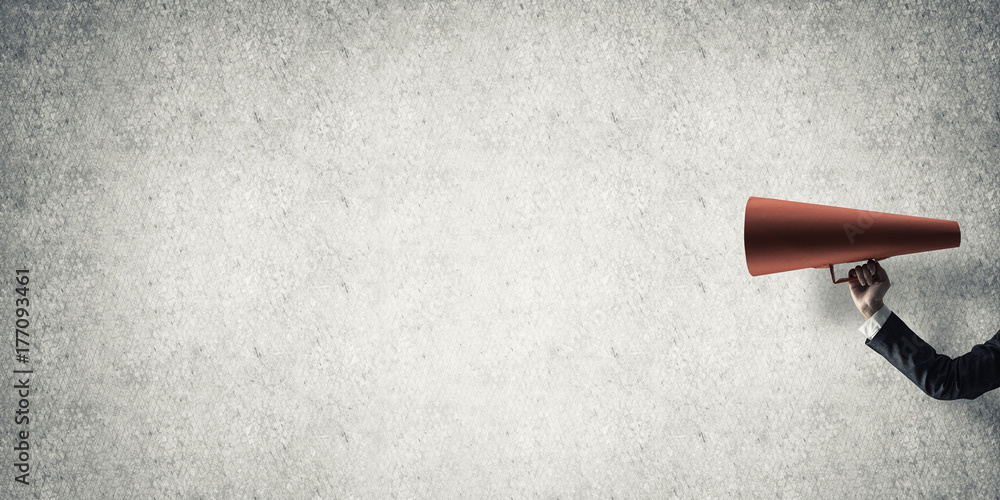 Hand of businesswoman holding red paper trumpet against concrete background