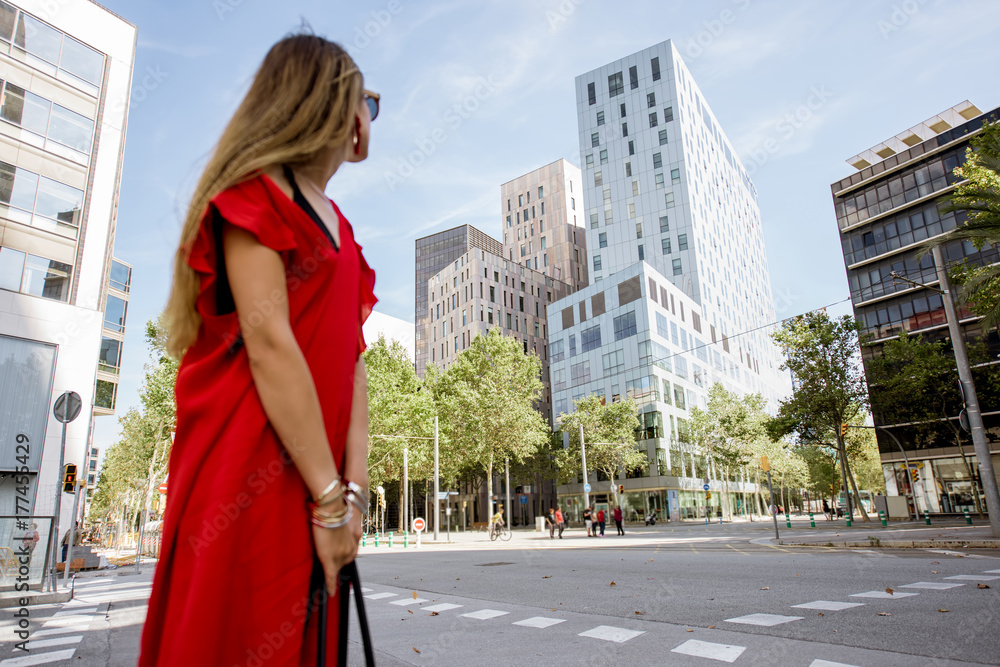 Woman in red dress looking on the modern office buildings in Barcelona. Image focused on the backgro