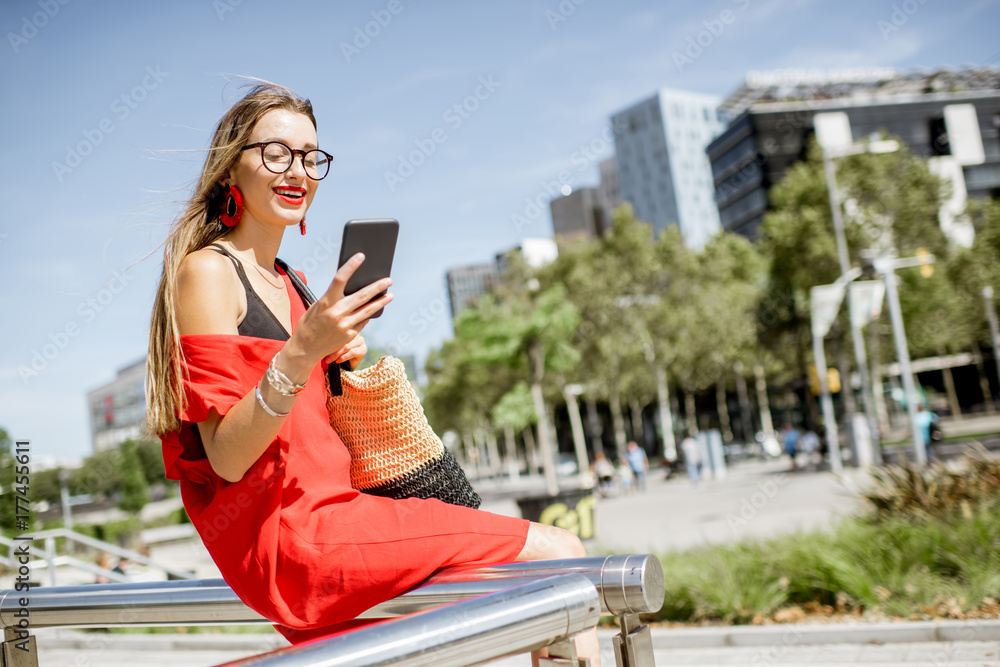 一位穿着红色连衣裙、拿着手机的商务女性坐在户外现代办公室的生活方式画像