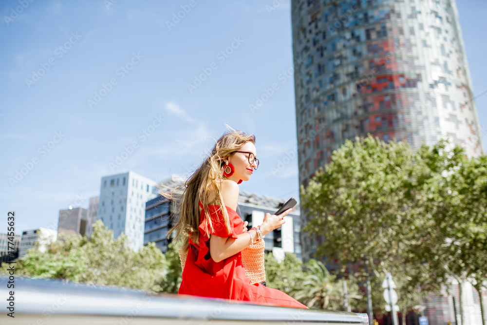 一位穿着红色连衣裙、拿着电话的商务女性坐在户外现代办公室的生活方式画像