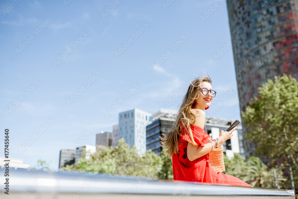 Lifestyle portrait of a business woman with phone in red dress sitting outdoors at the modern office