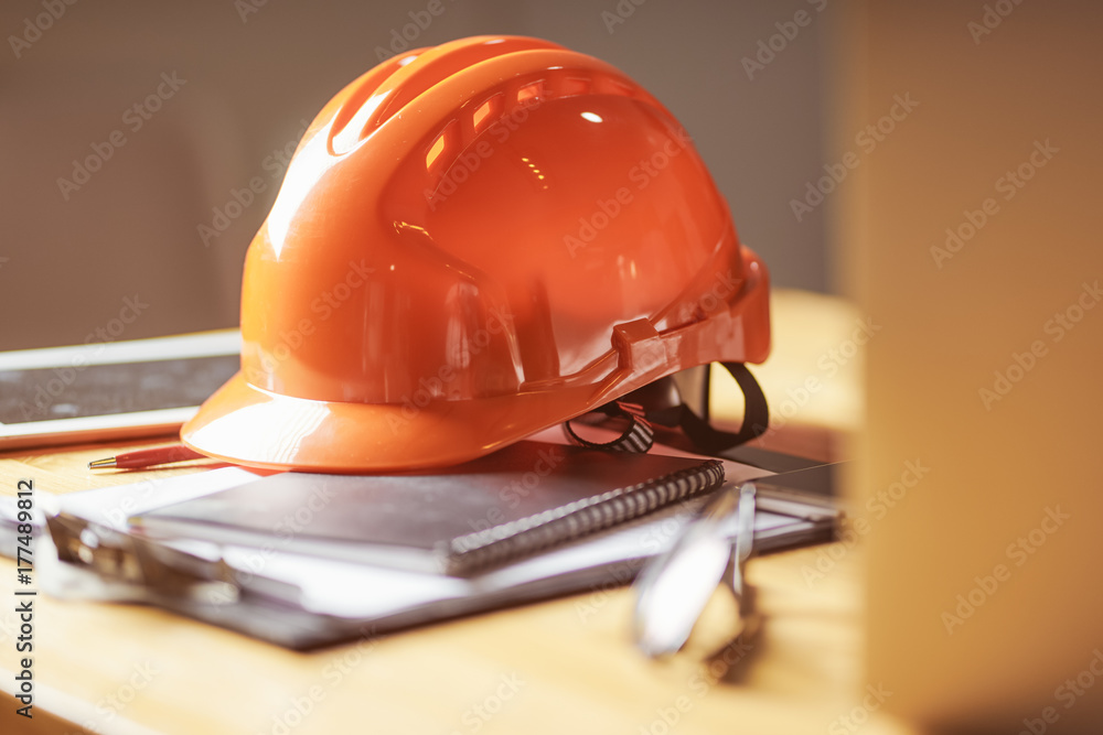 Laptop ,glasses, note book ,phone ,blueprint and orange safety helmet stacking on table at construct