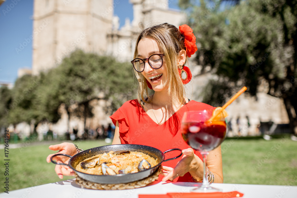 年轻女子穿着红色连衣裙，配上传统的巴伦西亚米饭——海鲜饭，坐在户外餐厅