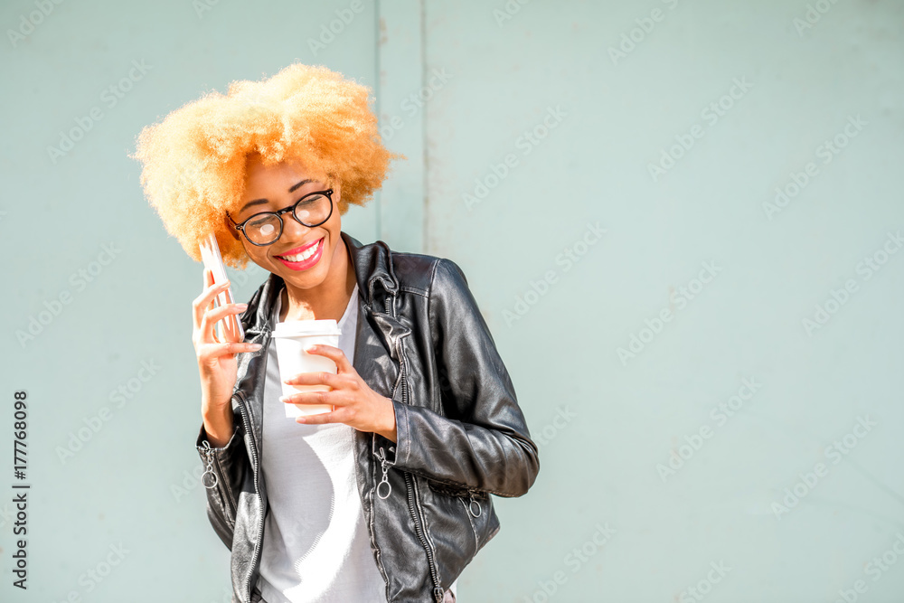 Lifestyle portrait of an african smiling woman in leather jacket talking phone on the green wall bac