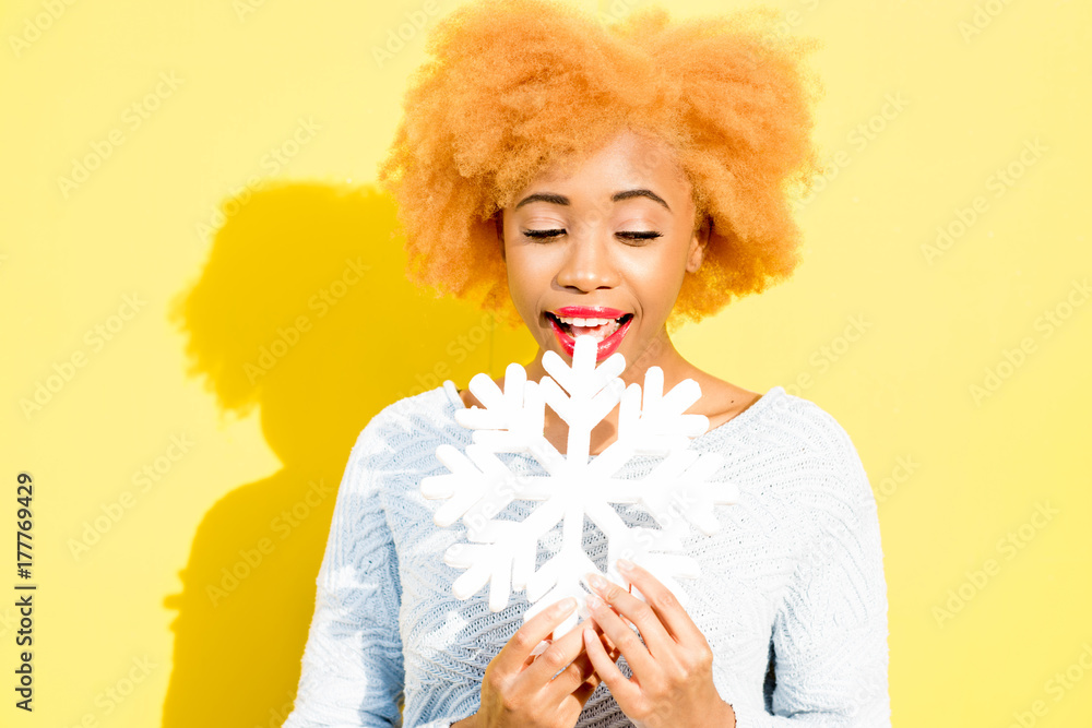 Portrait of a cute african woman in blue sweater holding an artificial snowflake on the yellow backg