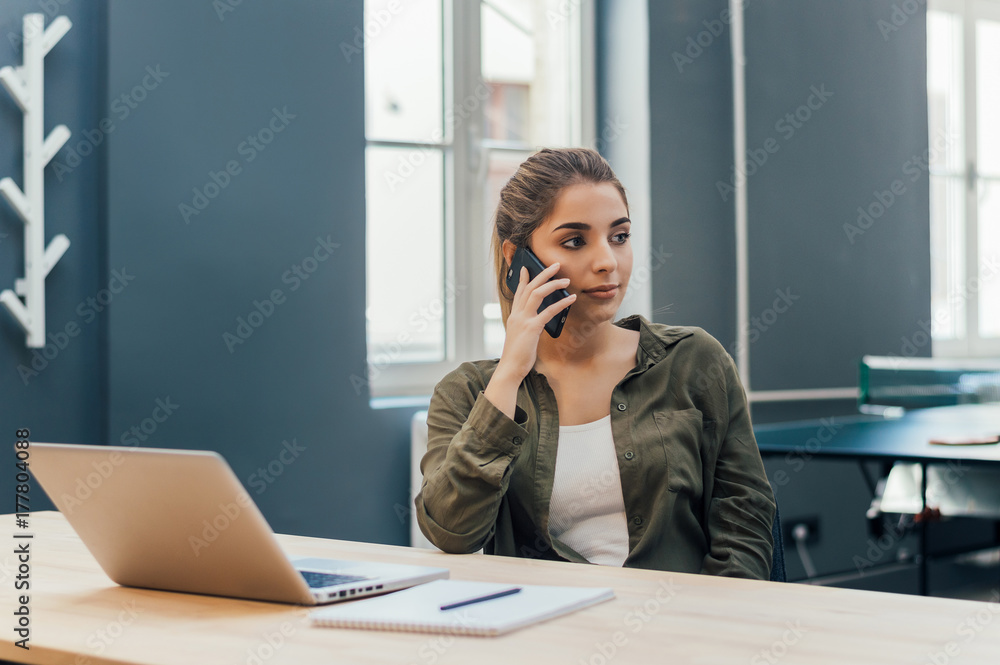 Young woman sitting in room with modern interior and talking on cellphone.