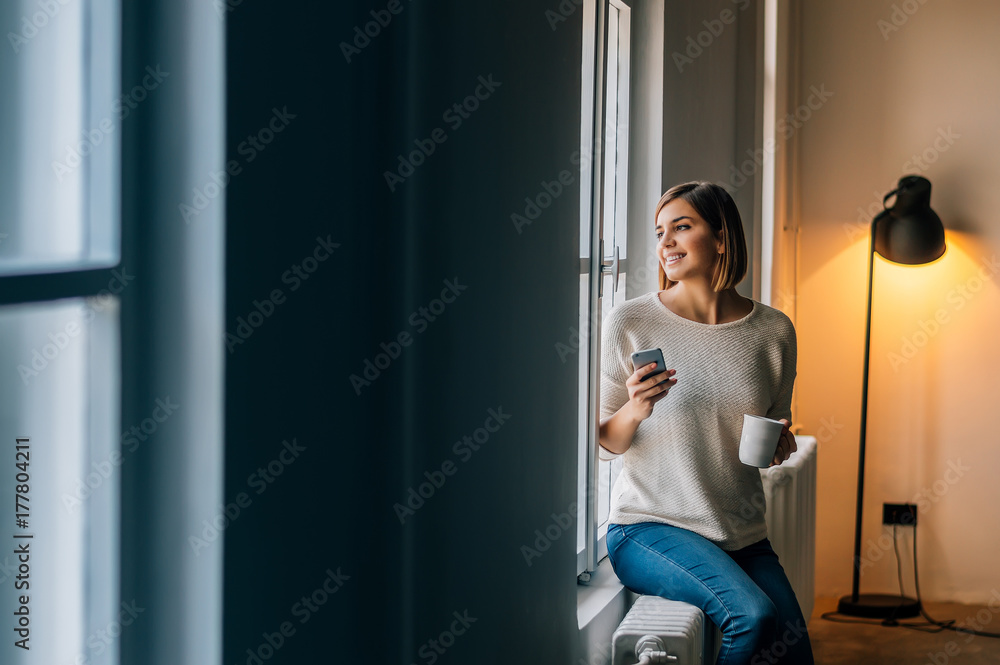 Beautiful smiling woman sitting near window and looking away.