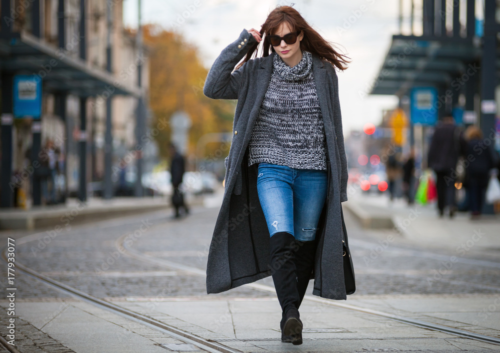 Trendy fashion woman in coat walking on the street, city scene