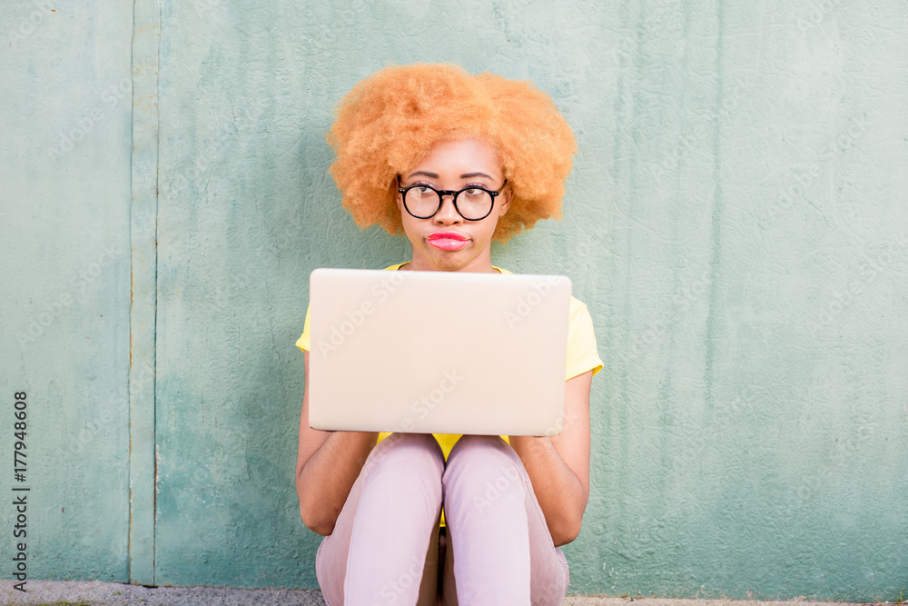 Beautiful african woman with curly hair working with laptop sitting on the green wall background