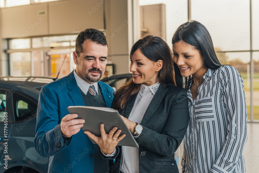 Shot of a handsome salesman showing documents to his happy clients at the dealership.