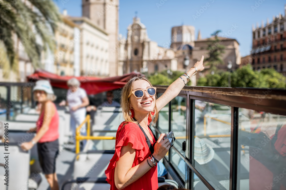 年轻快乐的女游客，穿着红色连衣裙，乘坐瓦伦西亚市的开放式旅游巴士游览。