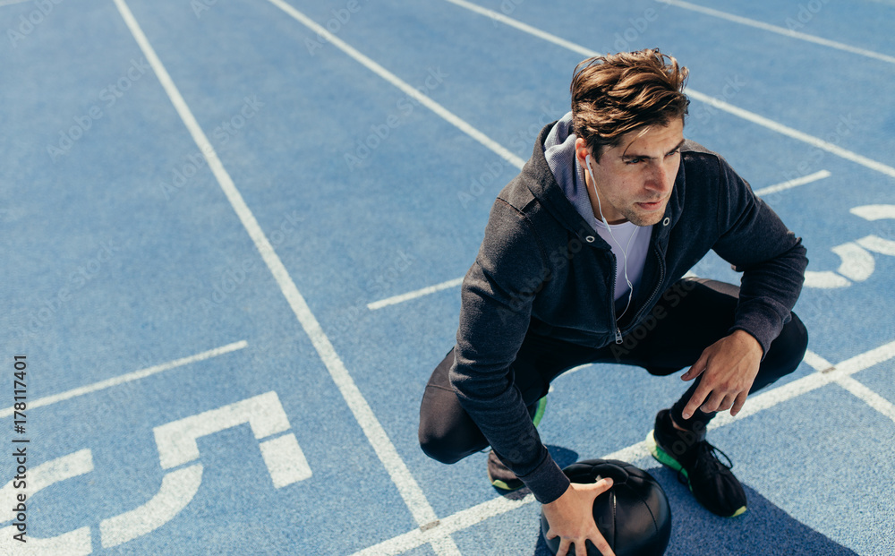 Athlete sitting on the running track with a medicine ball