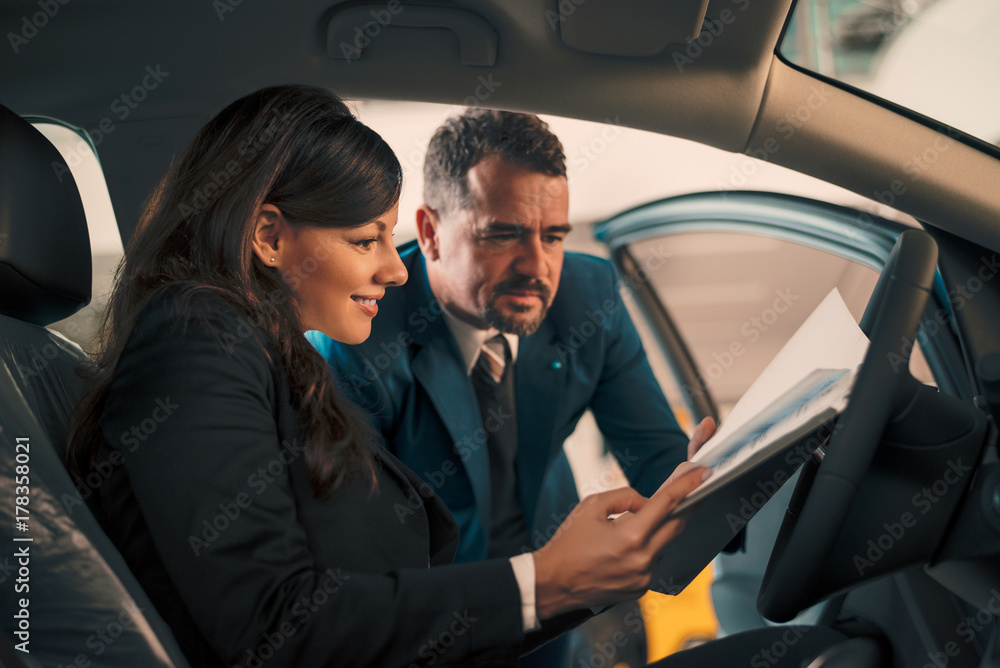 Happy woman inside car in auto salon with car dealer.