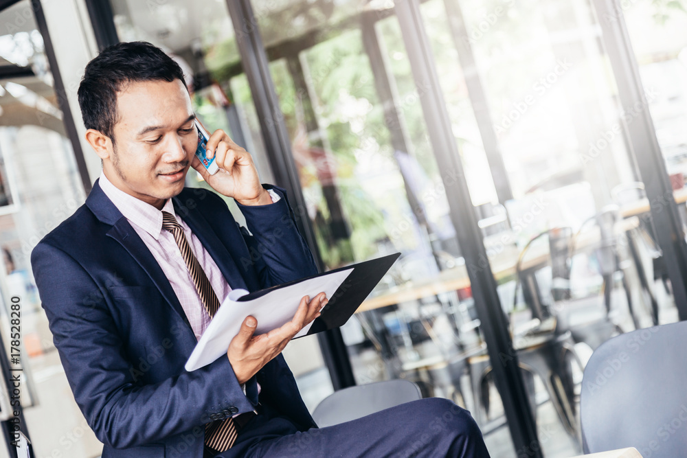 smart and handsome asian business man with suit working with smartphone and tablet outdoor location