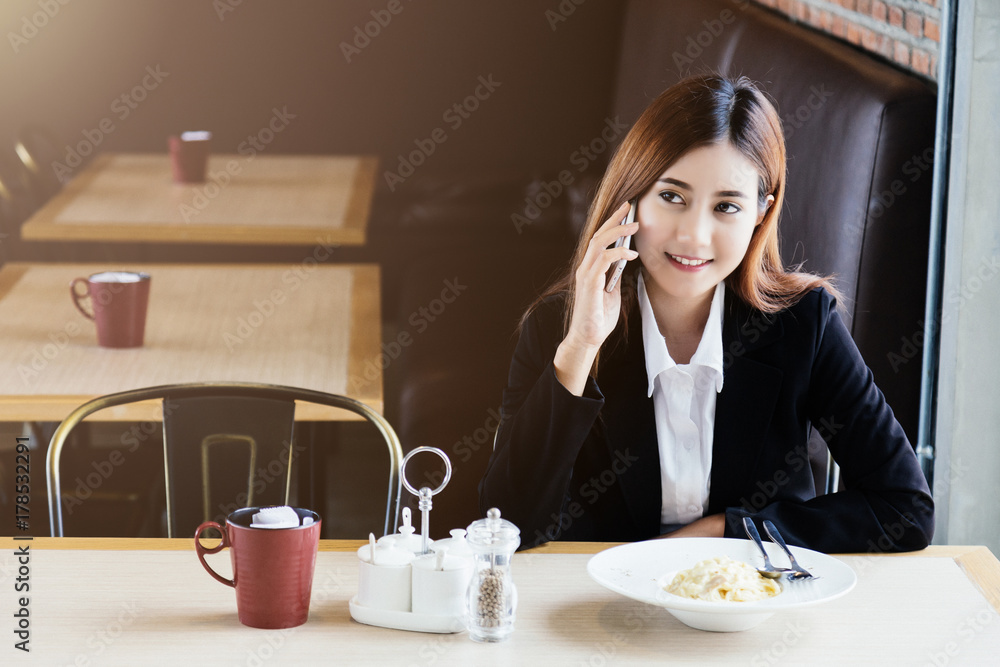 美丽的亚洲女孩在餐厅用智能手机等待时间