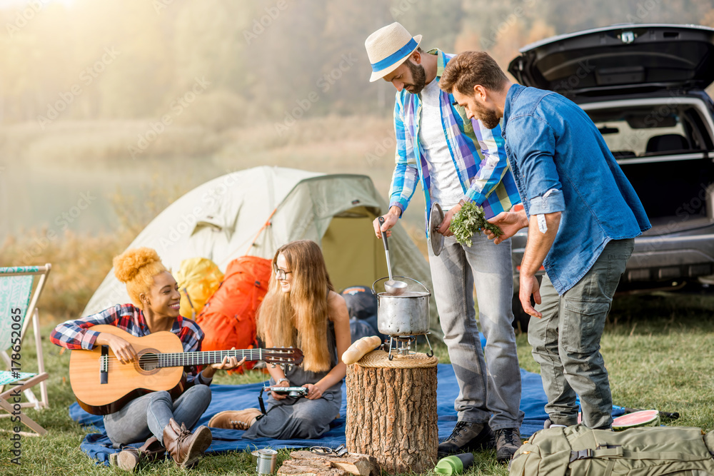 Multi ethnic group of friends dressed casually having a picnic, cooking soup with cauldron during th