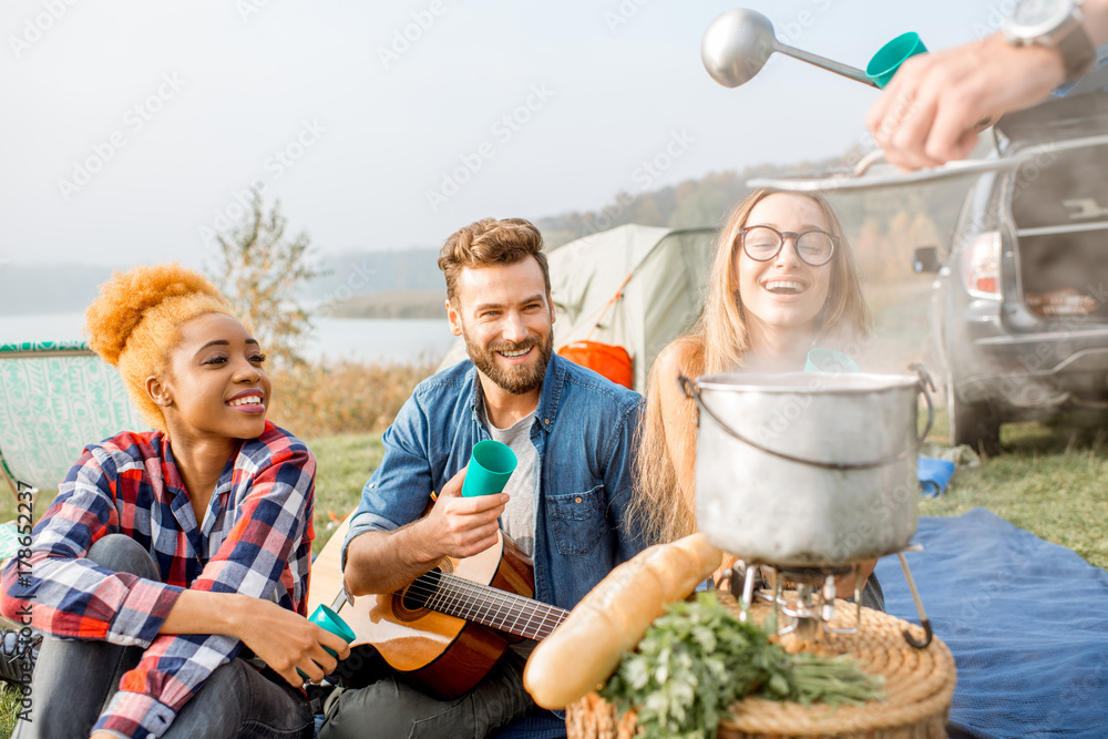 Friends having a tasty dinner with soup cooked in cauldron during the picnic at the camping