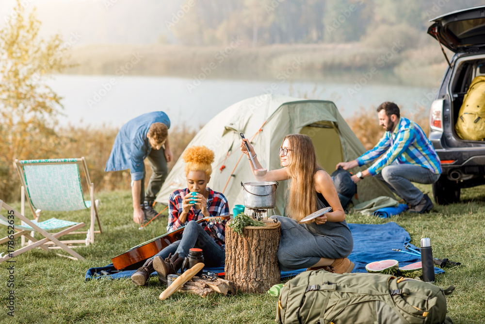 Multi ethnic group of friends dressed casually having a picnic, cooking soup with cauldron during th