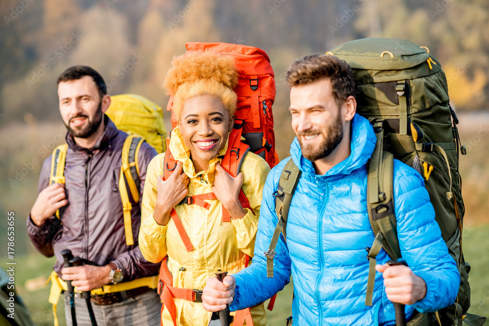 Multi ethnic friends in colorful jackets hiking with backpacks in the forest