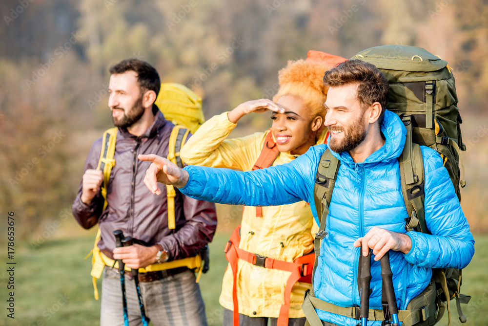 Multi ethnic friends in colorful jackets hiking with backpacks in the forest