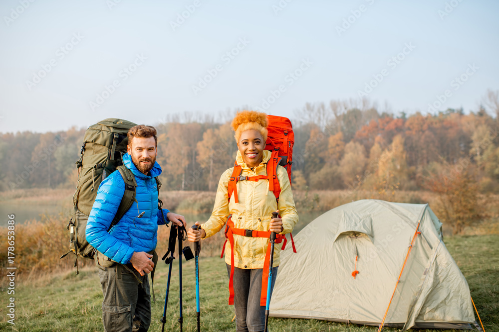 美丽的多民族夫妇背着背包和棍子站在露营地徒步旅行的肖像