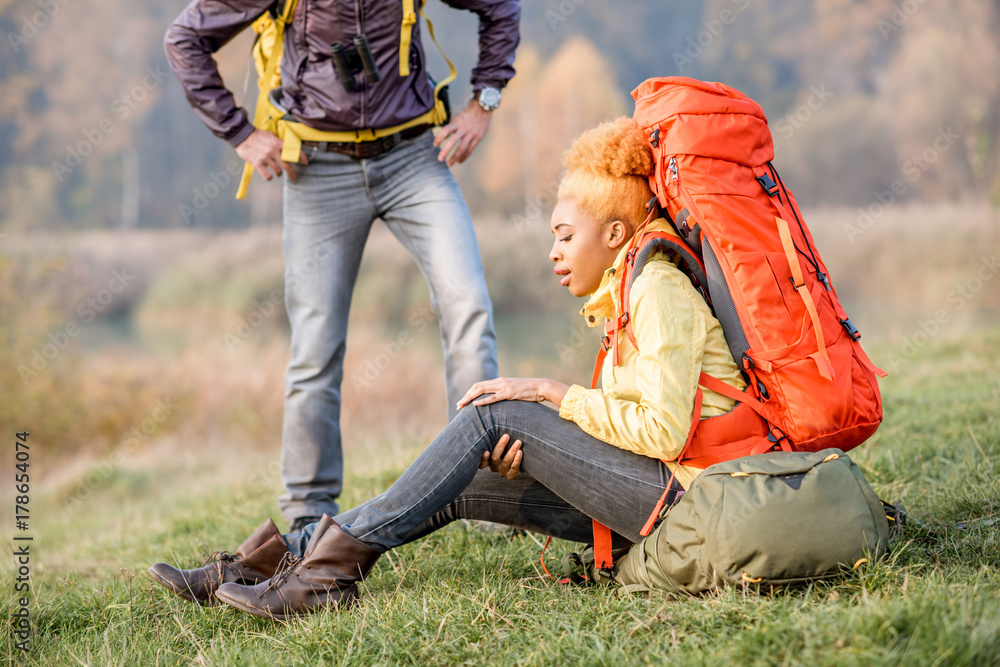 Young african woman with backpack having a trauma with knee hiking with friends outdoors