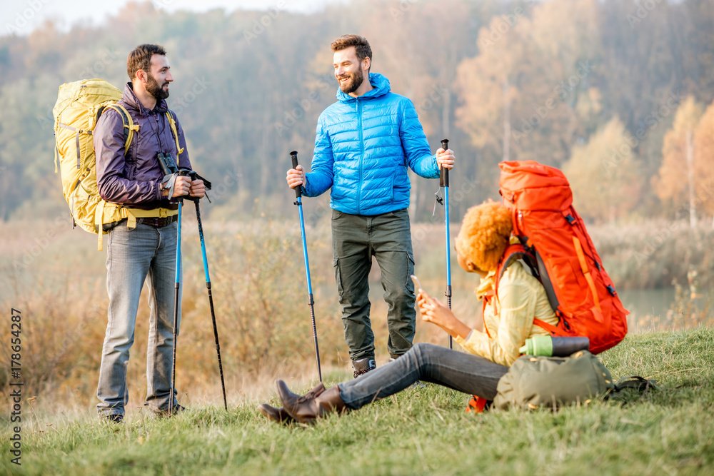 Group of friends in colorful jackets having a break with backpacks outdoors on the green lawn