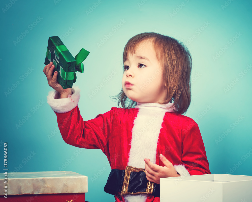 Happy toddler girl in a Santa costume with a gift box