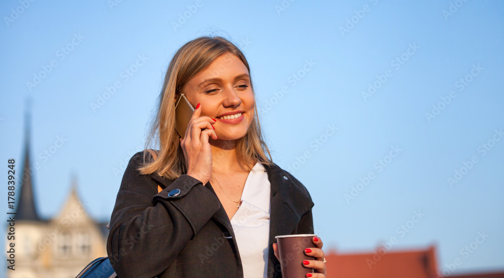 拿着咖啡杯的女孩在电话里聊天，走在街上