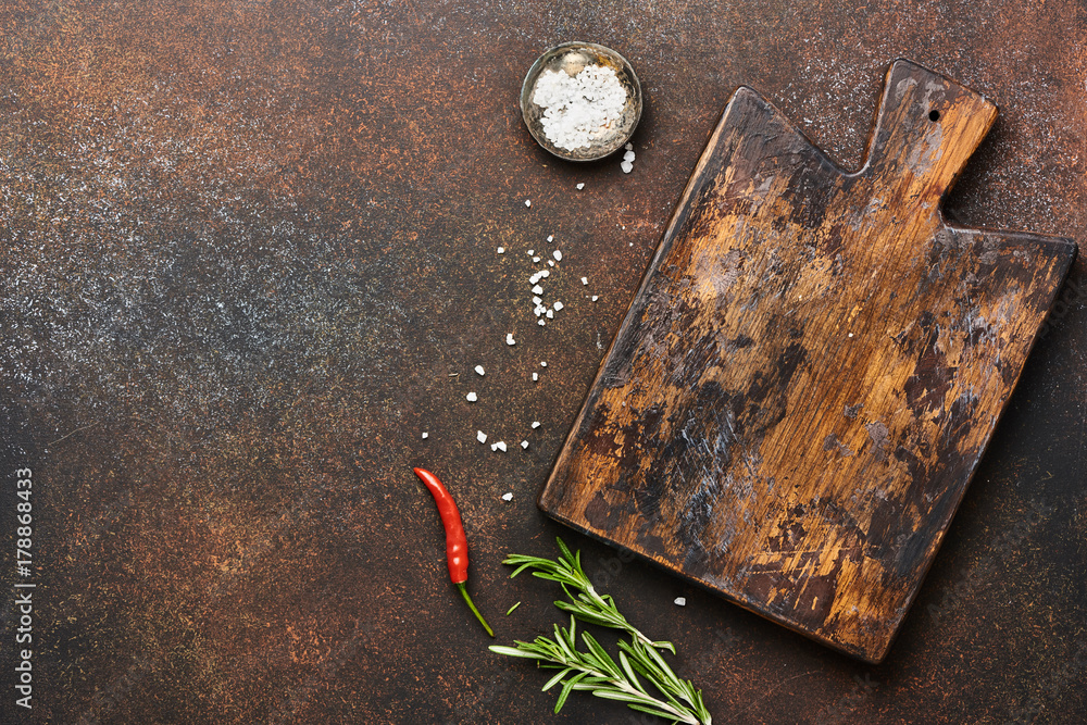 Wooden board with herbs, spices and salt on brown concrete background