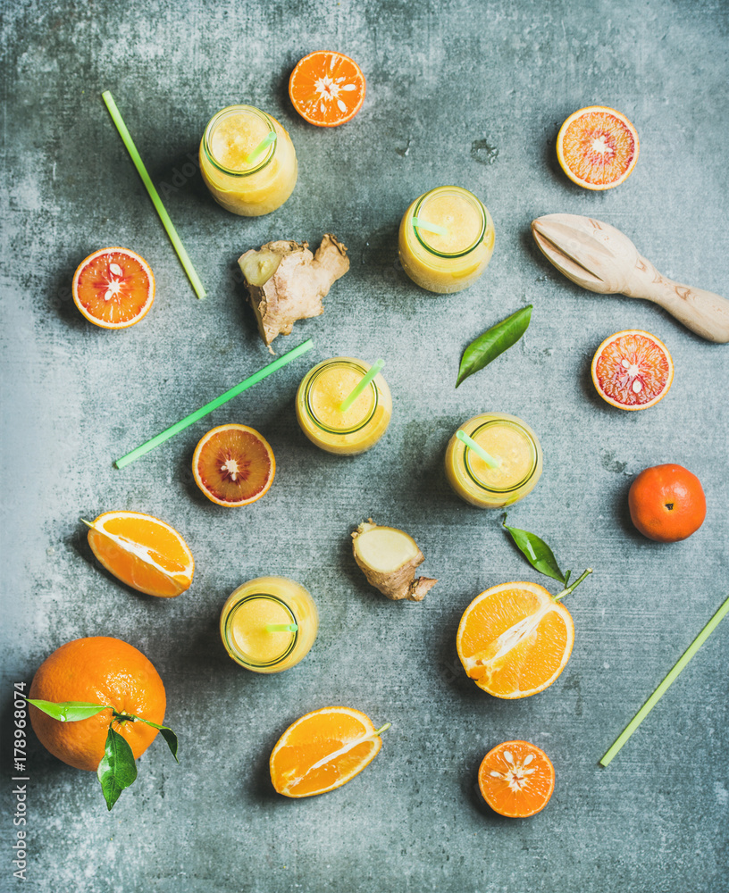 Healthy yellow smoothie with citrus fruit and ginger in bottles over grey concrete background, top v