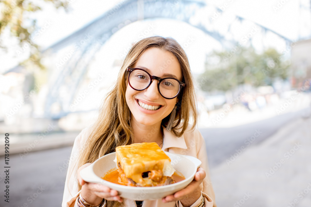 一位年轻女士坐在酒吧里享用传统的葡萄牙肉三明治Francesinha